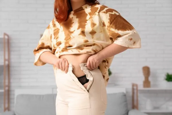 Image of woman trying to do her trousers up after pregnancy weight gain Scottish