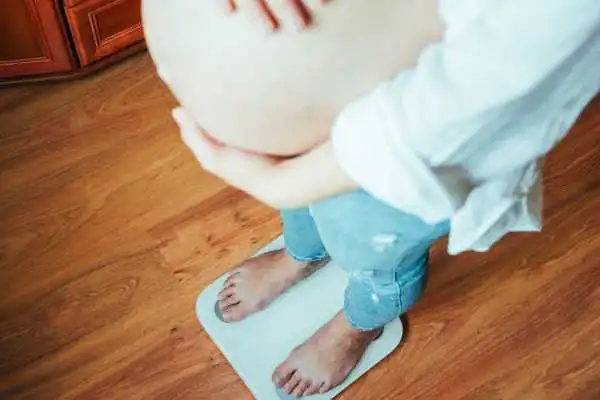 Image of woman weighing herself and experiencing weight gain through pregnancy Scottish